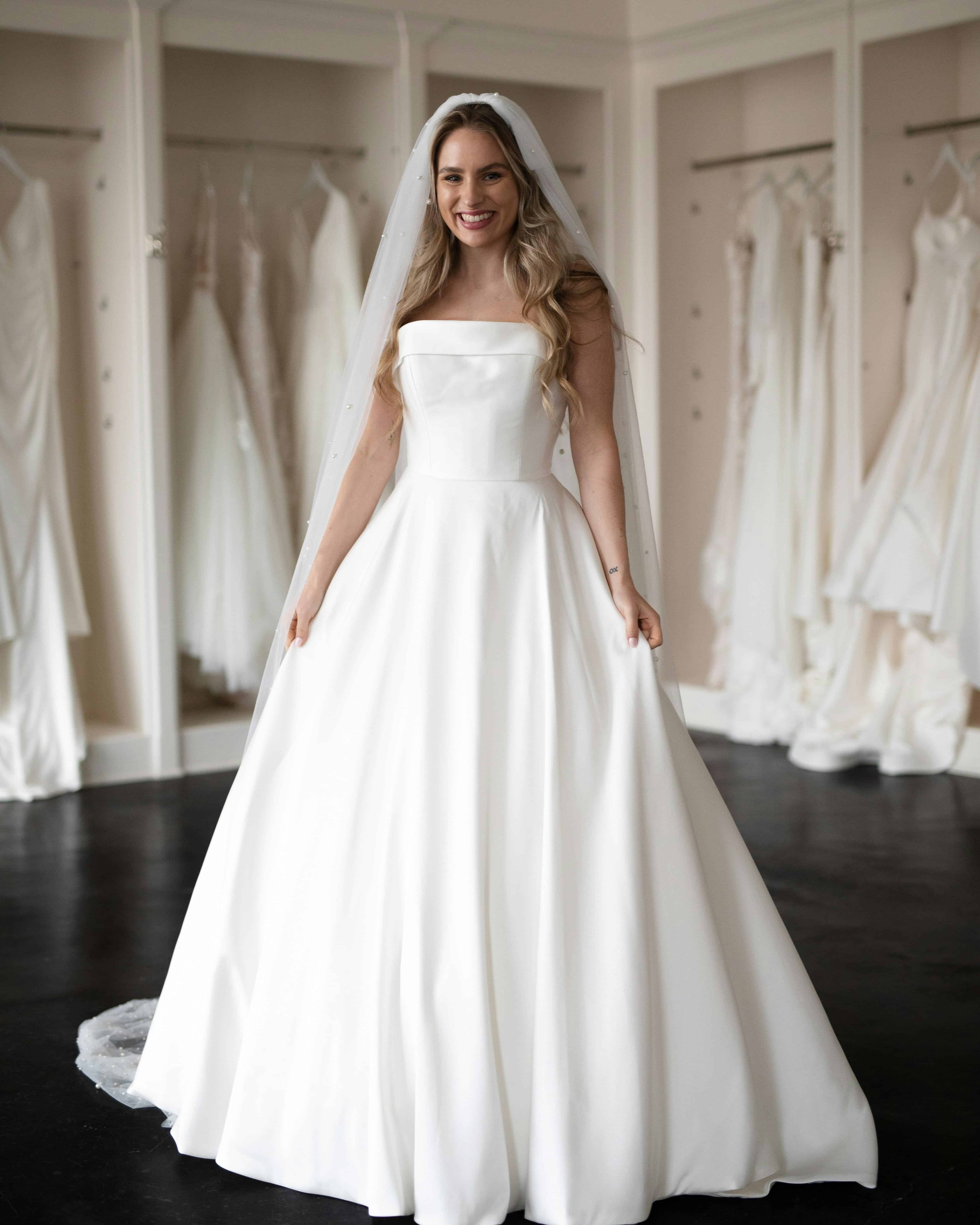 bridal-hair-and-dress-styling-inspiration-guide.jpg – Copy Happy bride trying on different wedding dresses in a bridal boutique.