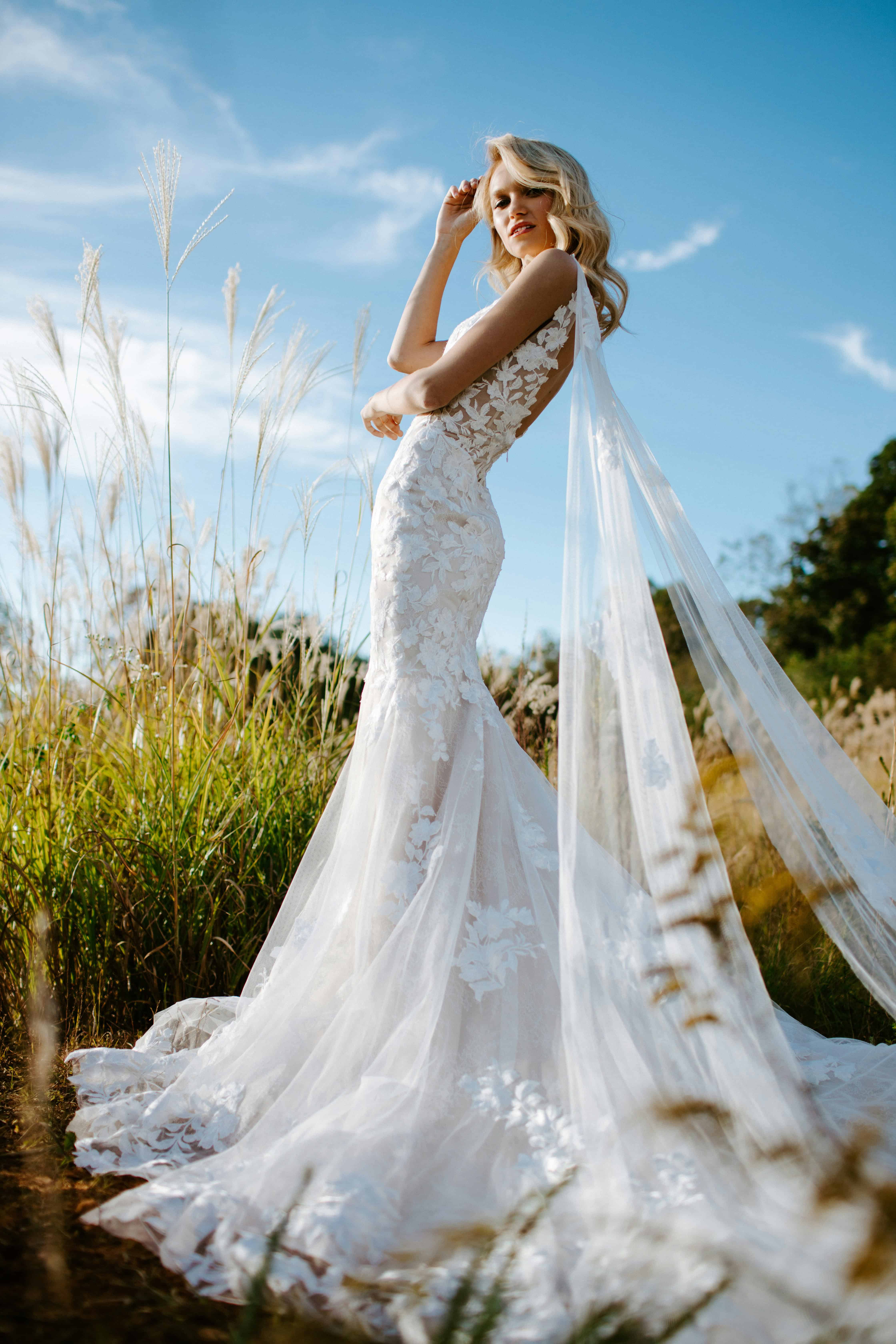 Blonde bride standing in soft sunlight with elegant bridal hair and natural wedding makeup.